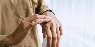A close up of a woman's hands, one holding a small jar of cream, the other rubbing the back of her hand.