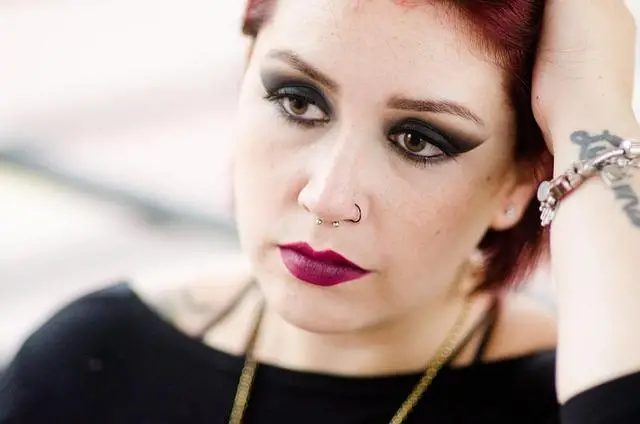 A middle-aged woman with make-up on eyes and lips, resting her head on her hand looking sad.