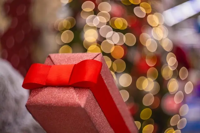 A single red-wrapped gift with a bow, a blurred Christmas tree in the background.