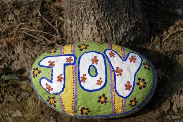 A painted green and yellow rock with the word "joy" in white letters.