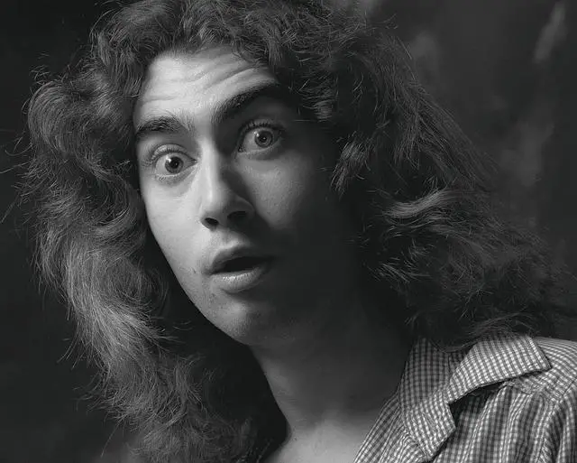 A black and white image of a young man with long curly hair looking astonished.