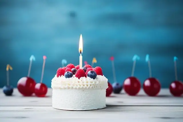 A white birthday cake with a single candle in the top with raspberries and blueberries on top.