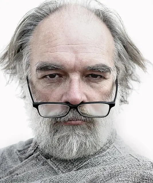 A man with grey beard and hair and glasses pulled down under his nose looking directly at us.