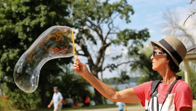 Susan herself with a large bubble wand and a giant bubble while at an outdoors event.