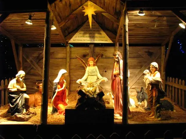 Ceramic nativity scene in a wooden stable and darkness all around.