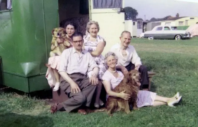 A photo from the 1950s showing an extended family of 5 with their 2 dogs outside their camper trailer.