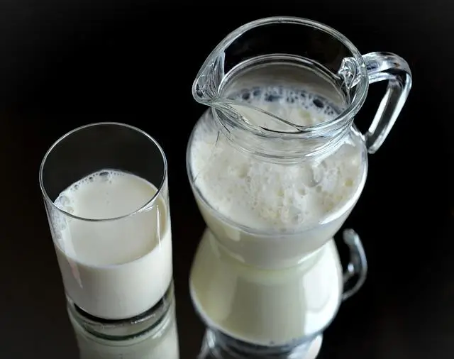 Milk in a clear glass and a clear jug on a black mirrored backdrop.