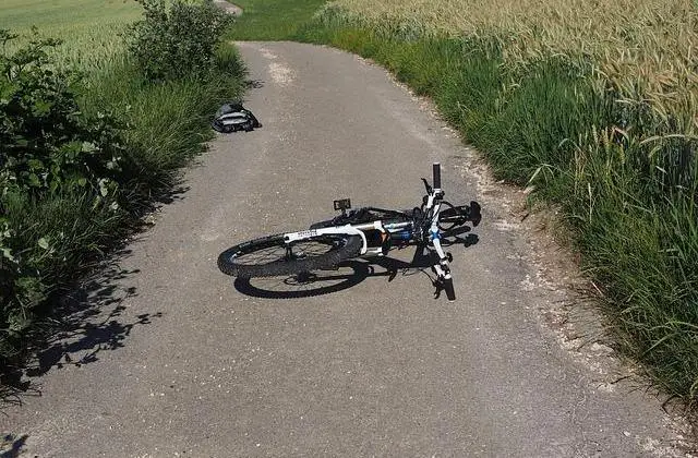 A bicycle on its side on a path with a backpack a little further away.
