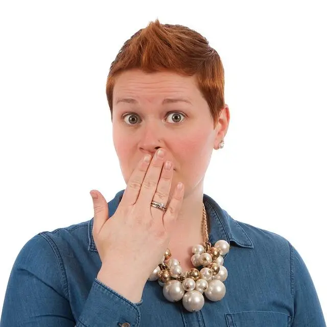 A woman with short red hair, fingers over her mouth looking surprised.