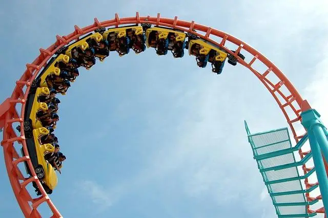 A steel roller-coaster with an orange track and yellow cars filled with people on the down side of a loop.