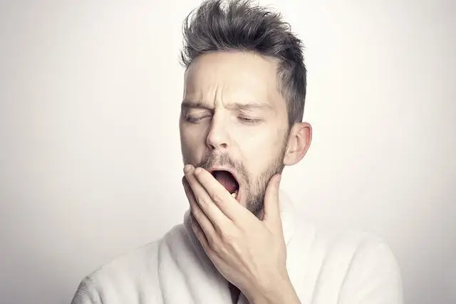 A young man with spikey hair covering up a big yawn with his left hand.
