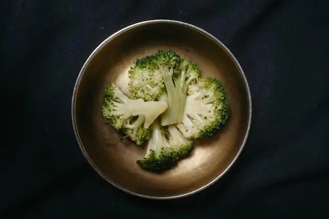 Four broccoli florets laying on their side in a plain brown bowl and black background.