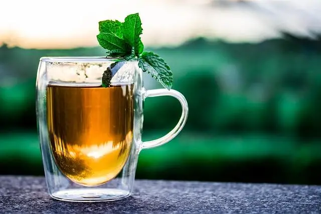 A clear mug of tea with a sprig of mint sticking out the top.