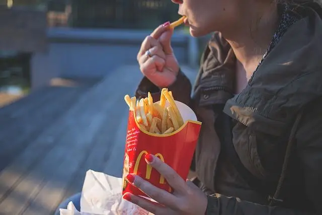 A close up of a woman holding a large container of McDonald french fries with one hand and eating one with the other.