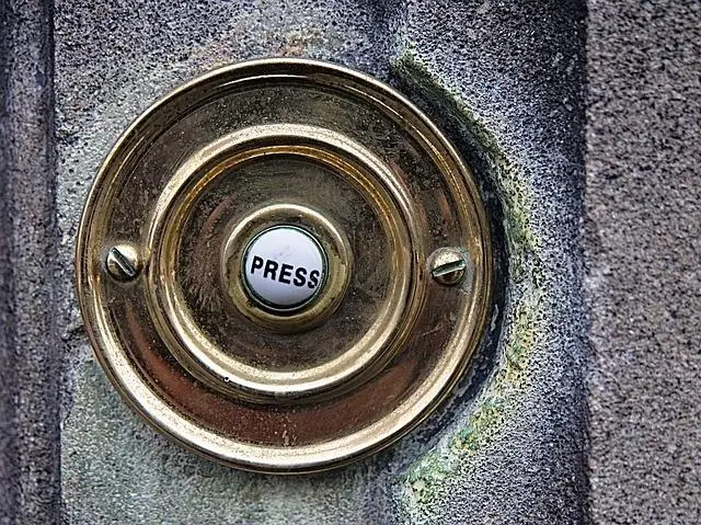 A round metal doorbell on a concrete wall.