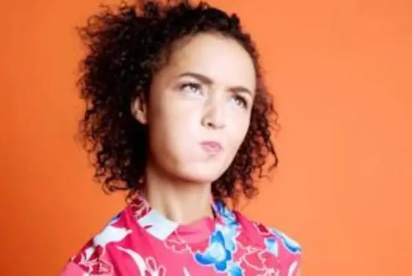 Woman with curly black hair, tongue in cheek, looking up and to her left.
