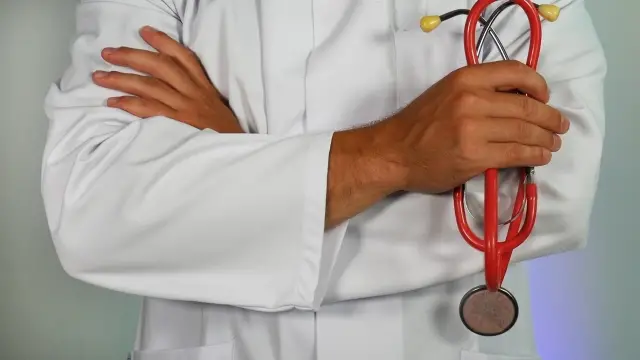 A close-up of a doctor standing with arms crossed holding a stethoscope.