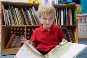Six year old child sitting on the ground looking at an open book.