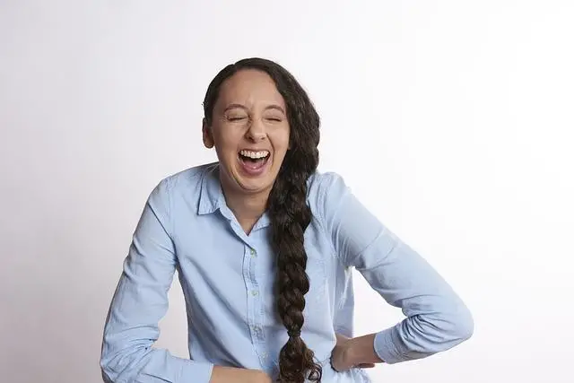 A woman in a blue shirt with a long braid holding her sides laughing.