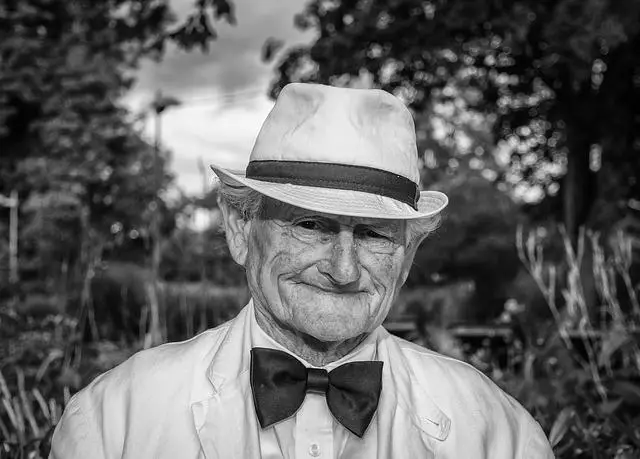 Black and white photo of a very old man dressed in white with a white hat and bow tie.
