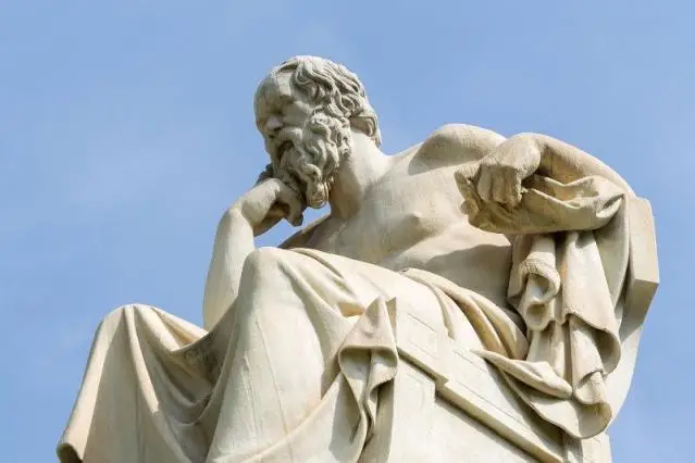 The famous statue of Socrates sitting with his hand on his cheek against a blue sky.