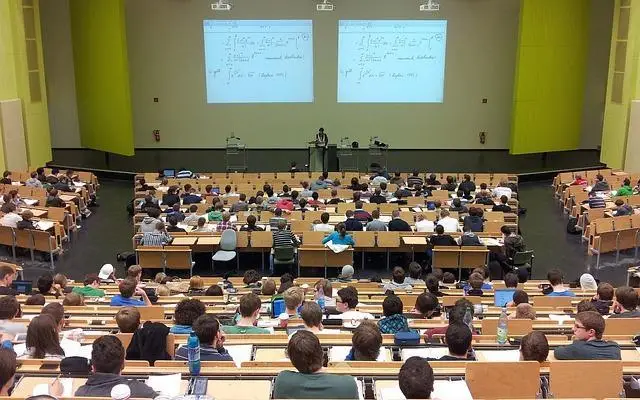 An image of a university lecture hall, from the back of the room, looking toward the professor at the front of the hall.