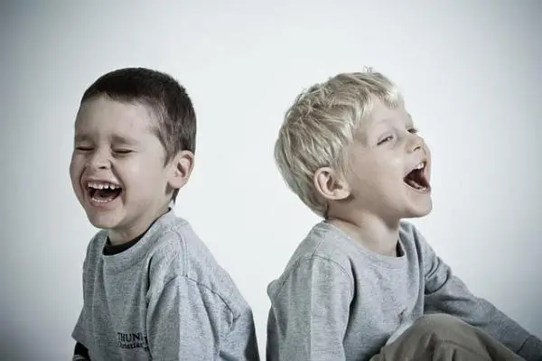 Two boys sitting back to back, both laughing.