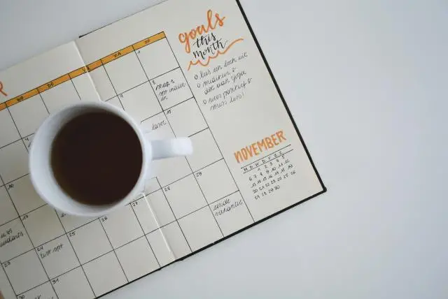 An open planner-scheduler on a desk with a cup of coffee sitting on top.