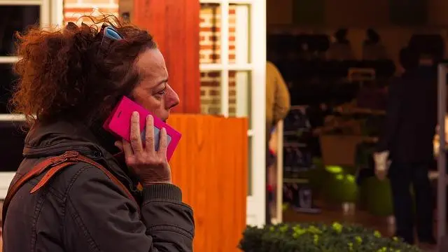 A middle-aged woman walking along a street with a pink phone to her ear.