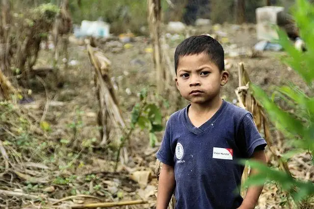 A young Guatemalan boy wearing a blue shirt with a World Vision sticker, short hair, clean face, looking directly at us.
