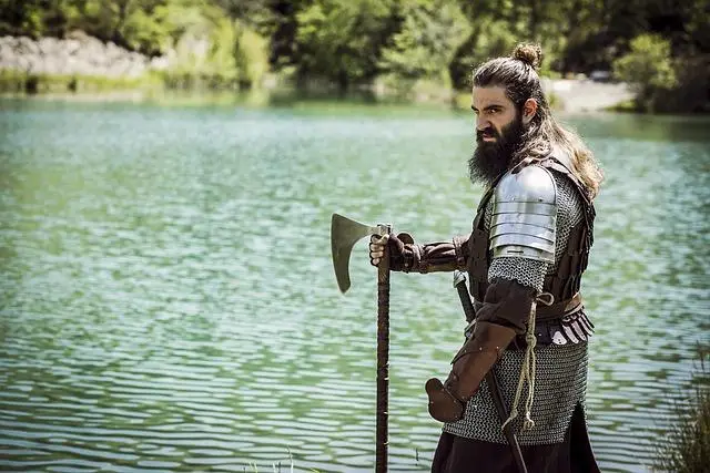 warrior man standing by a lake with his hand on his long axe.